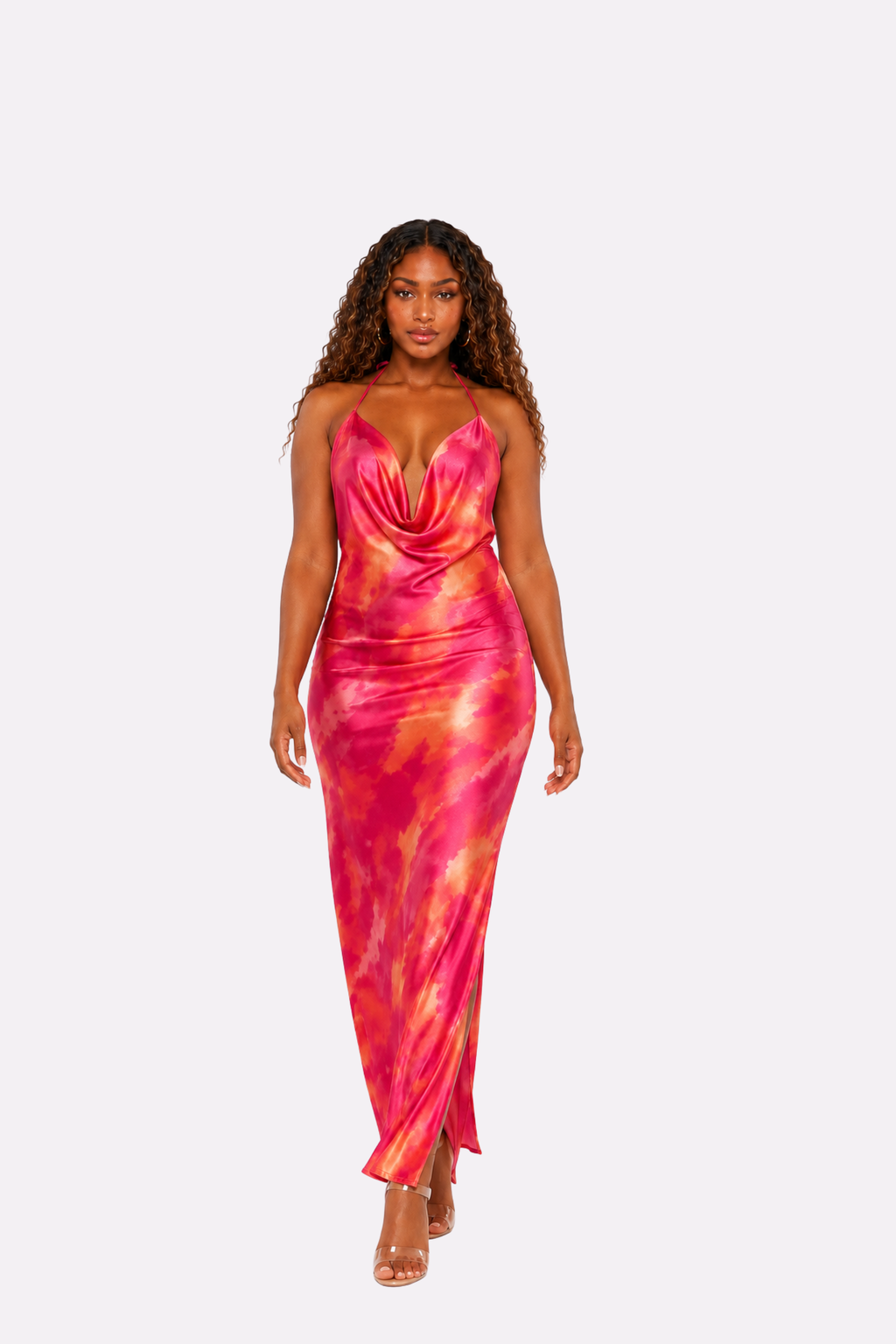 A woman modeling a sleeveless, floor-length satin gown with a vibrant pink, orange, and yellow tie-dye pattern against a solid light gray background.