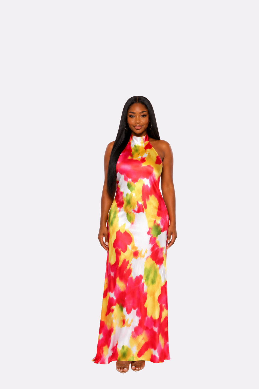 A woman modeling a sleeveless halter-neck maxi dress with a vibrant abstract floral print in red, yellow, green, and white, set against a solid light gray background.